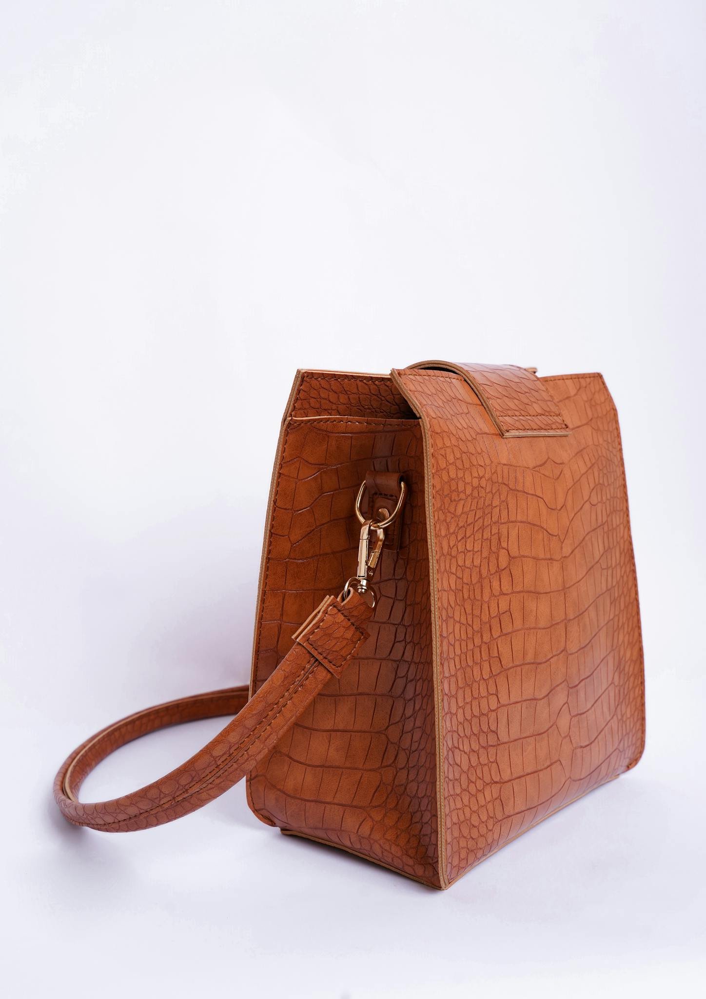 Brown textured leather handbag with strap against white backdrop, elegant and timeless accessory.